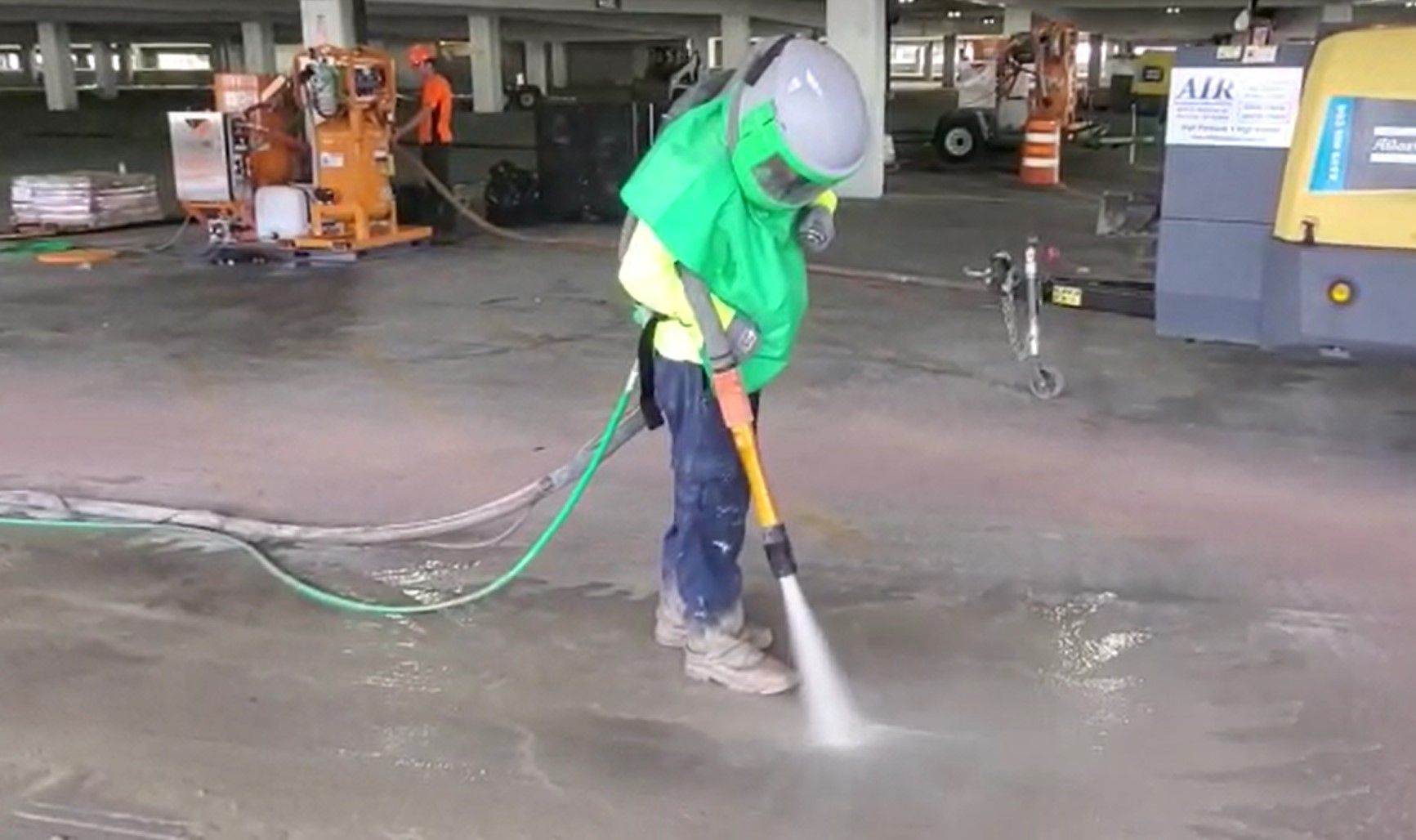 Blasting contractor using a silent blast nozzle in parking garage with blasting skid in background